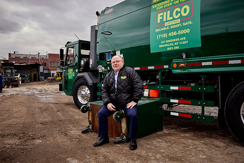 Domenic Monopoli sits in front of a green Filco Carting waste truck