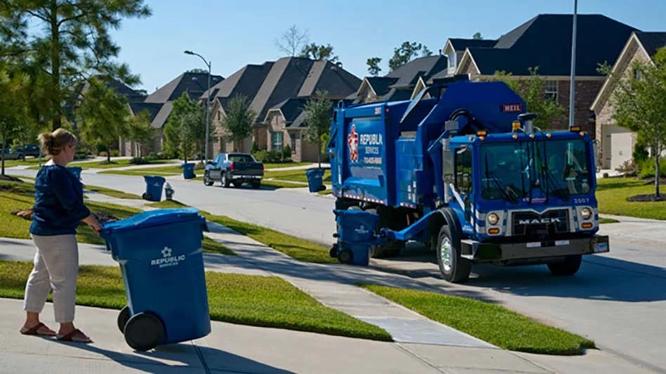 A Republic Services customer takes her cart to the curb as a collection truck approaches