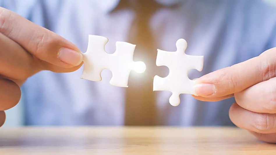 man in a blue shirt and tan tie holds a puzzle piece in each hand