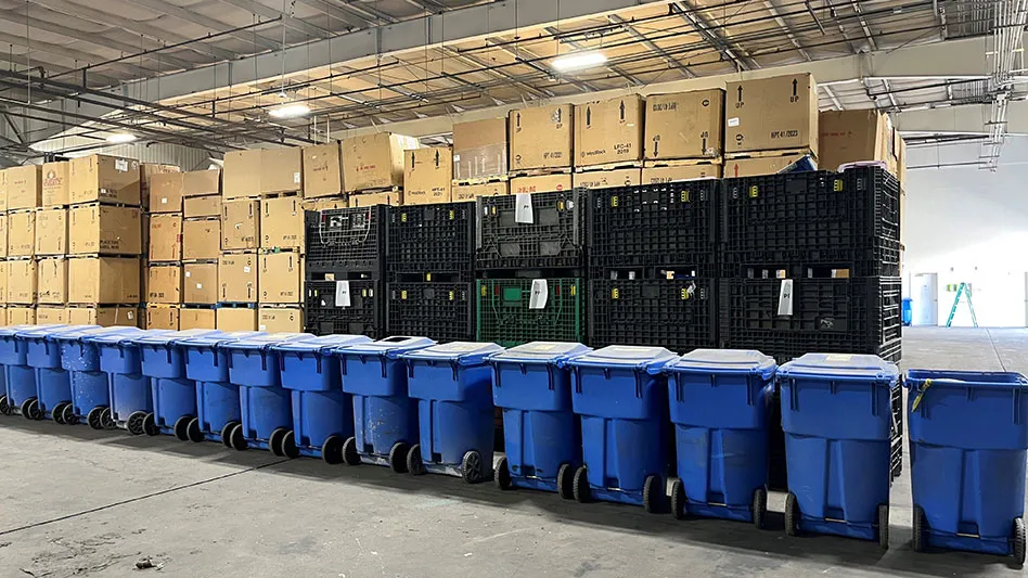 row of blue recycling bins lined up in front of brown corrugated boxes