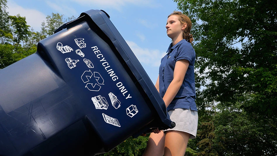 Young girl taking out the recycling bin to the curb against blue sky and trees