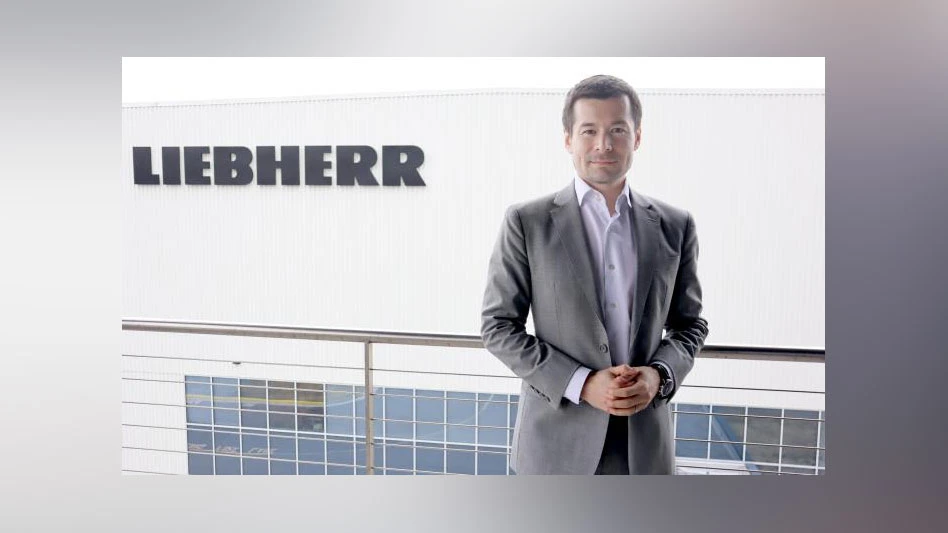 Photo of an Asian man in a suit standing in front of a Liebherr logo